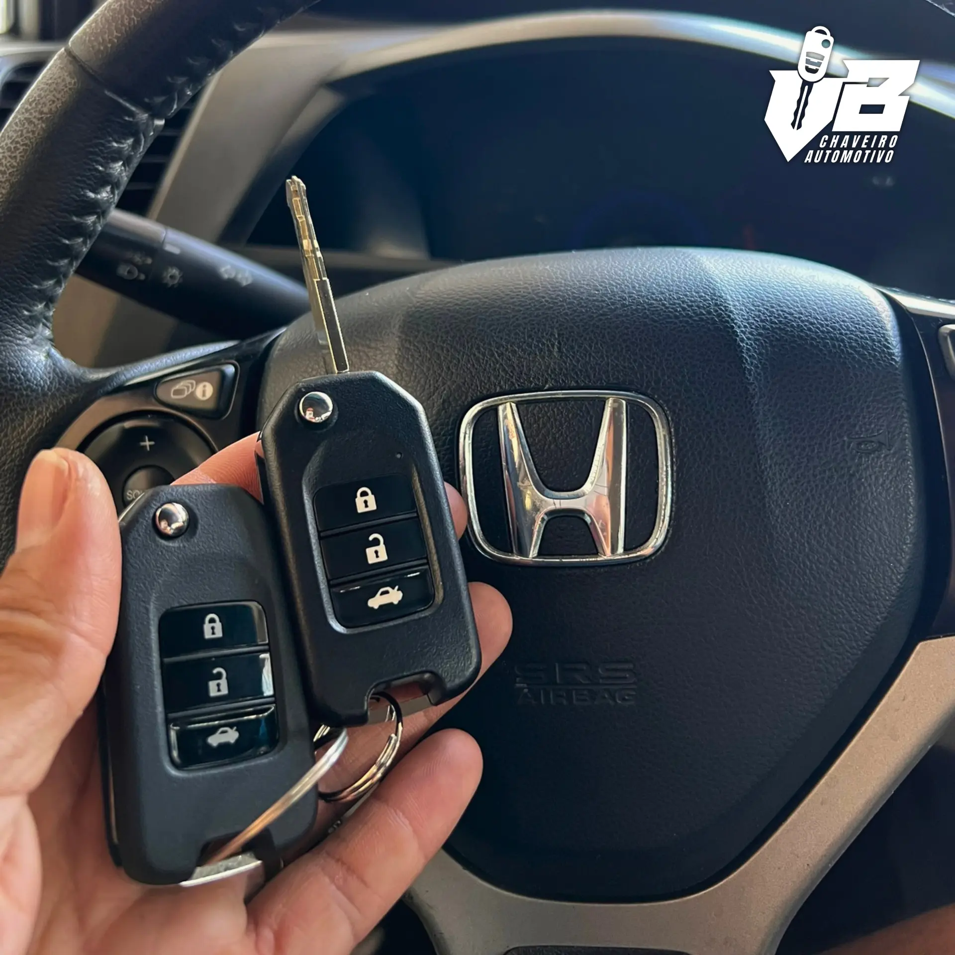 Duas chaves automotivas tipo canivete seguradas em frente ao volante de um veículo